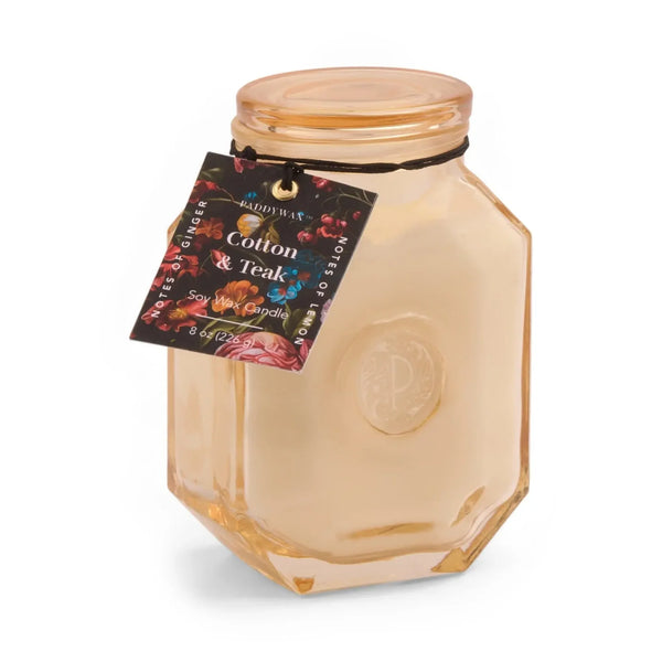 The 8oz Botanica Candle features cream-colored soy wax in a geometric light amber jar, embossed with a logo and finished with a black string tag labeled 