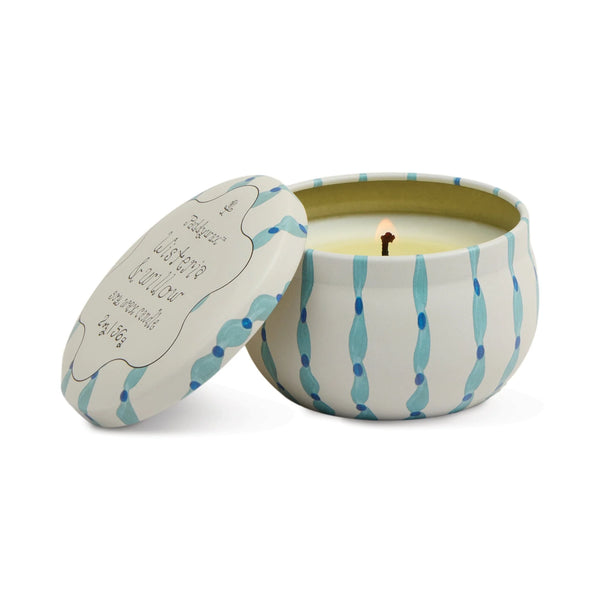 A lit Printed Tulip Candle Tin in a round, white and blue patterned container sits with its decorative lid beside it, hinting at fragrant notes like Cactus Flower or Bronzed Gardenia.